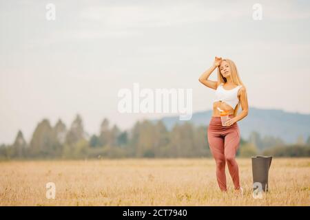 Schöne blonde Mädchen trinkt Wasser nach dem Sport Yoga auf Teppich im Park. Trainingskonzept Stockfoto