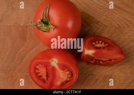 Eine ganze rote Tomate und zwei Scheiben Tomate Auf einem Holzbrett Stockfoto