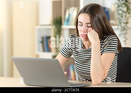 Gelangweilt teen mit einem Laptop verschwenden Zeit sitzen in ein Schreibtisch zu Hause Stockfoto