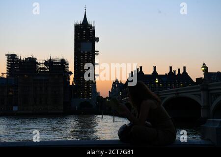 Eine Frau liest ein Buch an der Themse, während die Sonne über den Houses of Parliament in Westminster, London untergeht. Stockfoto