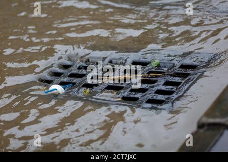Schmutziges Regenwasser fließt in einen Straßenregensturm. Stockfoto