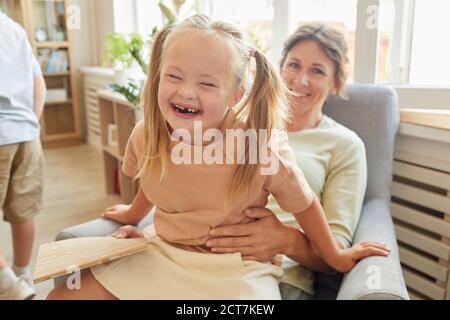 Portrait von niedlichen Mädchen mit Down-Syndrom lachen glücklich, während Spielen mit Mutter zu Hause Stockfoto