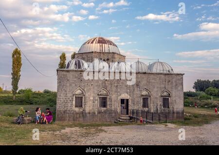 Bleimoschee, Shkoder, Albanien. Eine alte und alte Moschee steht auf einem grünen Rasen rund um den Wald und gutes Wetter draußen. Lokale Leute sitzen in der Nähe Stockfoto