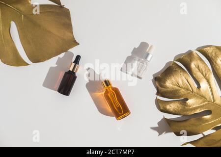 Weiße, orange und schwarze Serumflaschen auf weißem Hintergrund. Trending goldenen Zweige der Monstera. Kosmetisches Modell. Platzieren Sie, um Text, Bilder einzufügen. Oben vi Stockfoto