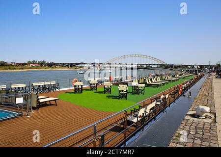 Nijmegen, Niederlande - September 18. 2020: Blick von der Uferpromenade über leeres Kreuzfahrtschiff auf dem waal mit Bogenbrücke waalbrug Hintergrund Stockfoto