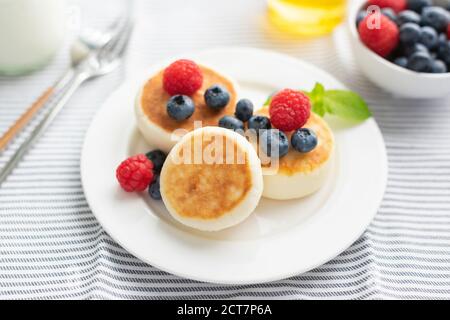 Syrniki, Quark fritters mit Beeren auf einem weißen Teller serviert. Gesundes Frühstück Stockfoto