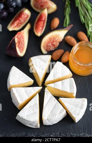 Camembert oder Brie Käse mit Feigen, Honig und Mandeln auf schwarzem Schiefertafel Stockfoto