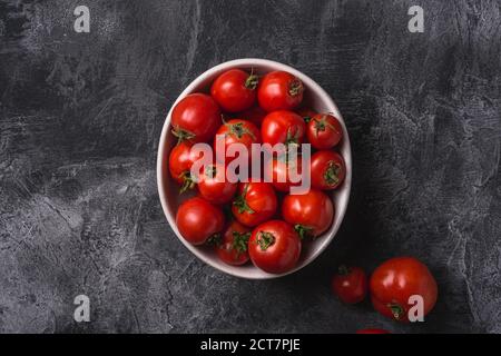 Frische reife Tomaten in Schüssel auf dunklem Betongrund, Draufsicht Stockfoto