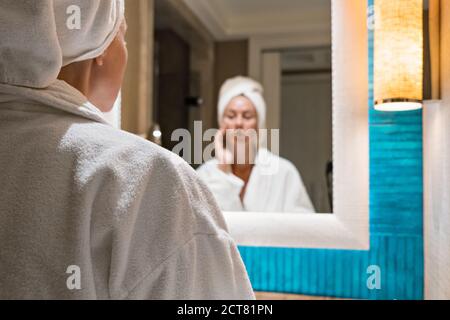 Schöne Frau im Bademantel steht vor der Badezimmerspiegel Stockfoto