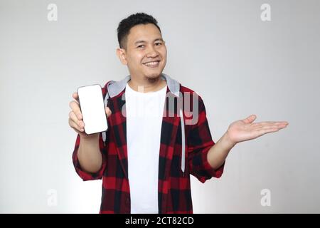 Porträt von jungen asiatischen Mann präsentiert Smartphone-Mockup Mit fröhlichem fröhlichem Ausdruck Stockfoto