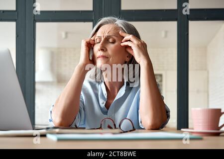 Müde gestresste alte reife Geschäftsfrau, die an Kopfschmerzen bei der Arbeit leidet. Stockfoto