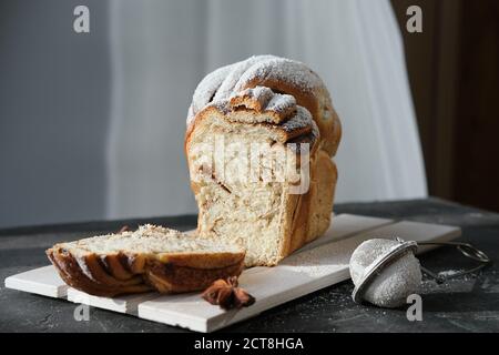 Ziehen Sie Zimt Wirbel Brot auf Holzgestell. Schneiden Sie traditionelle süße Brot Laib mit Zucker gepudert. Würziges Brot gebacken. Winter Saison Gebäck. Selektive Konzentration Stockfoto