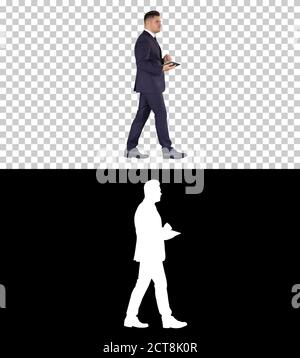 Eleganter junger Geschäftsmann mit seinem PC-Tablet beim Gehen, Alp Stockfoto