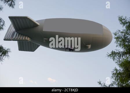 Fliegender Blimp mit Schild und Baumzweigen mit blauem Himmel. Stockfoto