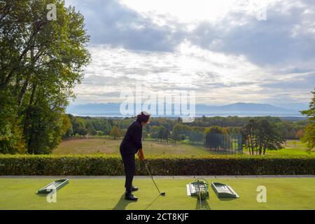 Frau auf der Driving Range mit Panoramablick über den Genfer See und die Berge in der Schweiz. Stockfoto