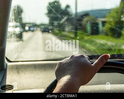 Am Lenkrad fährt eine Hand ohne Maniküre einer müden Frau mittleren Alters, ein Auto mit schmutzigem Glas in die Vororte, selektiver Fokus Stockfoto