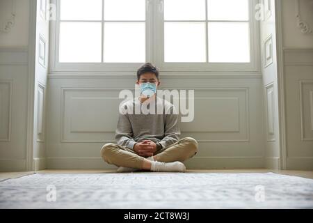 Junger asiatischer Mann in Quarantäne sitzt auf Boden Beine gekreuzt Blick auf die Kamera Stockfoto