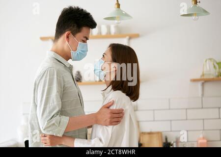 Seitenansicht der jungen asiatischen Paar trägt Maske halten und Einander anschauend Stockfoto