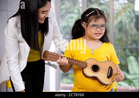 Asiatische Lehrer lehren Ukulele Mädchen mit Down-Syndrom. Konzept behindertes Kind lernen in der Schule. Stockfoto