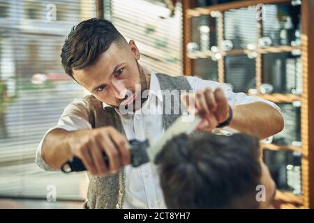 Konzentrierter Friseur, der an einem neuen Haarschnitt für seinen Besucher arbeitet Stockfoto