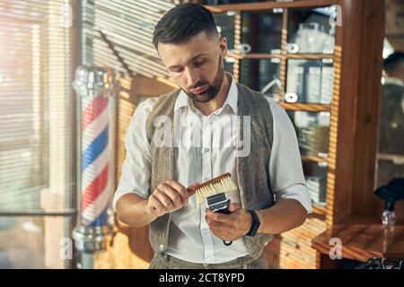 Geschickter Friseur, der seinen elektrischen Trimmer mit einer Bürste reinigt Stockfoto