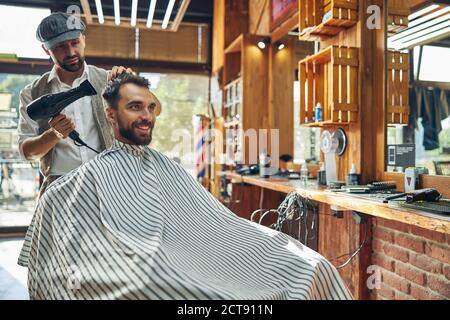 Fröhlicher junger Mann, der sein Haar in einem Friseurladen getrocknet hat Stockfoto