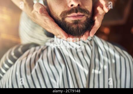 Junger Mann mit Friseur Tuch bedeckt mit seinem Bart gepflegt Stockfoto