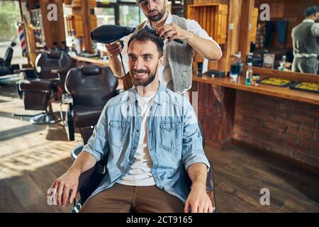 Fröhlicher Kunde eines Friseurshops, der sein Haar getrocknet hat Stockfoto