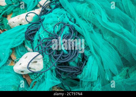 Nahaufnahme Stapel von grünem Nylon Multi bunte helle Fischnetze mit Stücken von weißen Korallen und alten Seilen in Fischerdorf. Stillleben Hintergrund Stockfoto