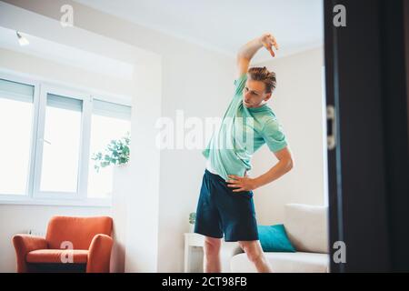 Kaukasischer Mann Stretching und Aufwärmen, bevor zu Hause basiert Fitnessstudio mit Sportkleidung im Wohnzimmer Stockfoto