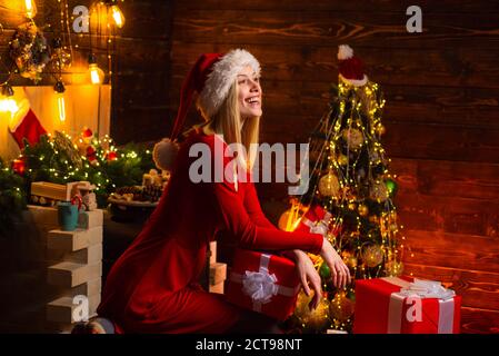 Glücklich lächelnd junge blonde Frau in rotem Kleid und Weihnachtsmann Hut auf Weihnachten dekoriert Hintergrund. Weihnachten im süßen Zuhause feiern. Weihnachten Stockfoto