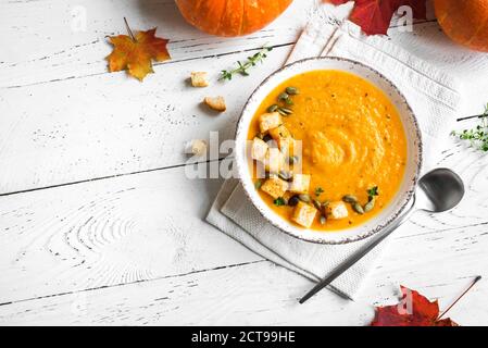 Kürbissuppe mit Croutons und gerösteten Kürbiskernen auf weißem Holztisch, Draufsicht, Kopierraum. Saisonales Herbstgericht - würzige Kürbis- und Karottensuppe Stockfoto