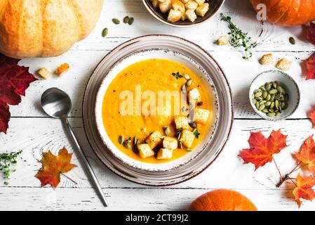 Kürbissuppe und Bio-Kürbisse auf weißem Holztisch, Draufsicht. Saisonales Herbstgericht - würzige Kürbis- und Karottensuppe. Stockfoto