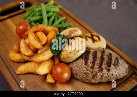 Ein köstliches Steak, Pommes und grüne Bohnen auf einem Holzschneidebrett Stockfoto