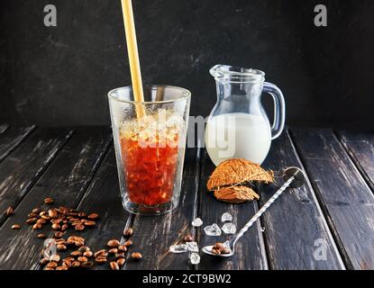 Eiskaffee im Thai-Stil mit Kokosmilch und Kaffeebohnen auf schwarzem Holzhintergrund. Stockfoto