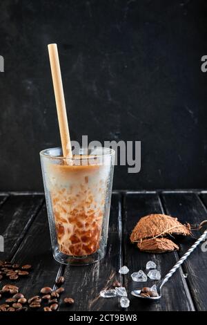 Eiskaffee im Thai-Stil mit Kokosmilch und Kaffeebohnen auf schwarzem Holzhintergrund. Stockfoto