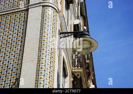 Ecke eines typischen alten Gebäudes im Zentrum von Lissabon (Portugal). Bunte Keramikfliesen (Azulejos) mit geometrischem Muster und einer hängenden Laterne. Stockfoto