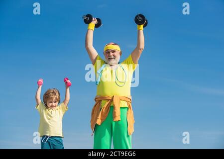 Sportler Großvater und gesundes Kind mit Hantel Übung. Kinder wiederholen Übung nach Großvater. Kind, das eine Hantel hebt. Stockfoto