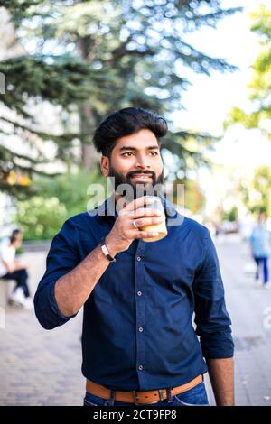 Junger indischer Mann trinkt Kaffee aus wiederverwendbarer Tasse im Freien. Stockfoto