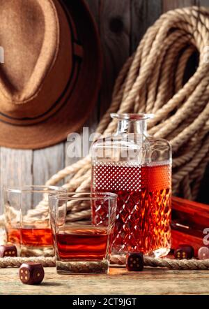 Starker Alkoholiker und Würfel auf einem alten Holztisch. Im Hintergrund sind ein Hanfseil und ein Männerhut. Stockfoto