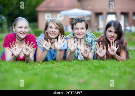 Drei Mädchen und ein Junge, die zusammen die Wort Teenager auf ihre Handflächen zeigen Stockfoto