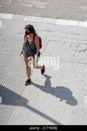 Junge Frau mit Schutzmaske, die in einer Straße läuft, während sie mit ihrem Handy Musik hört. Stockfoto