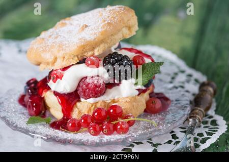 Windbeutel mit Sahne und Beeren auf Holztisch, Nahaufnahme Stockfoto