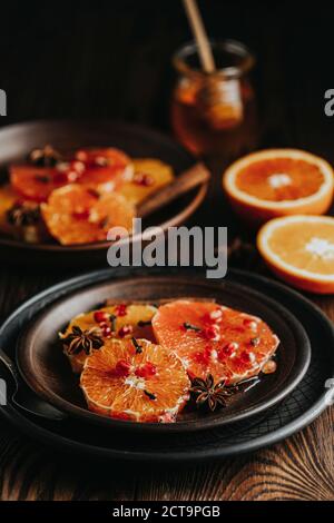 Orangefarbenes Dessert mit Weinhonig oder Ahorn-Sirup und Ingwer-Gewürz, verzierten Granatapfelbeeren. Wunderbar süße, reiche und frische Speisen. Dunkles, rustikales Bac Stockfoto