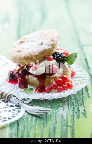 Windbeutel mit Sahne und Beeren am grünen Tisch, Nahaufnahme Stockfoto