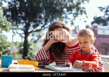 Glückliche Mutter und Kleinkind Lesung Lift-the-Flap Kinderbuch in der Garten Stockfoto