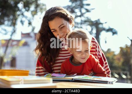 Glückliche Mutter und Kleinkind Lesung Lift-the-Flap Kinderbuch in der Garten Stockfoto