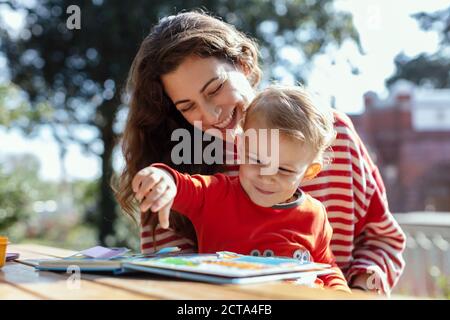 Glückliche Mutter und Kleinkind Lesung Lift-the-Flap Kinderbuch in der Garten Stockfoto