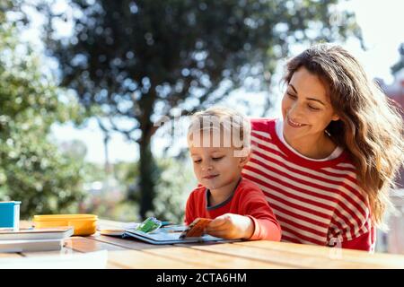 Glückliche Mutter und Kleinkind Lesung Lift-the-Flap Kinderbuch in der Garten Stockfoto