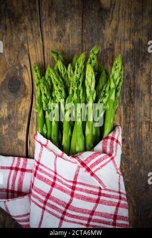 Bund grüner Spargel, Spargel Officinalis, eingewickelt in Küchentuch liegen auf dunklem Holz Stockfoto